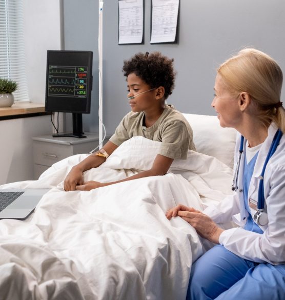 Sick boy talking to his family online Sick little child sitting in bed together with his doctor and talking online with his family on computer at hospital ward